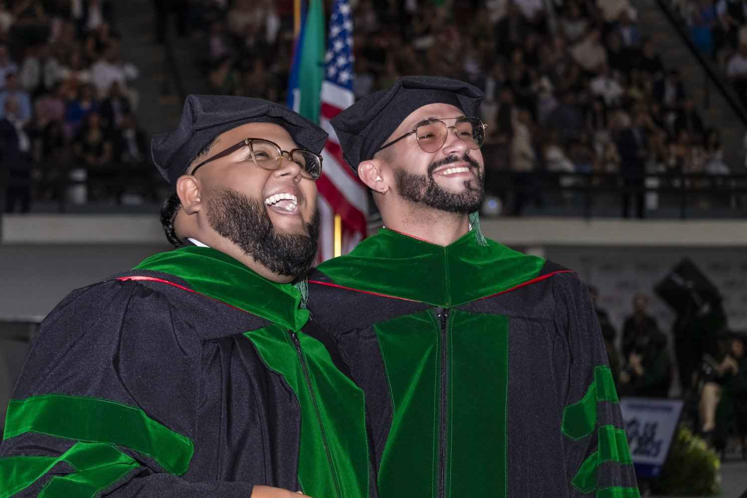 Two men in graduation robes share a joyful moment in celebration of their achievement